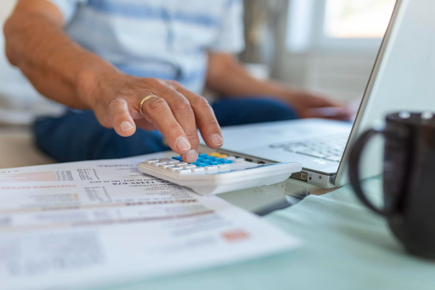 Imagem com pessoa fazendo cálculos na calculadora, notebook e contrato, simbolizando a revisão de dívidas bancárias.